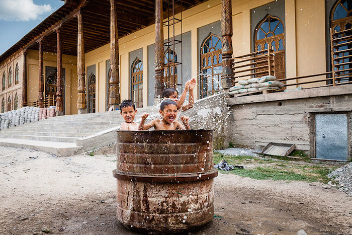 Tajik children playing in drum of water outside mosque
